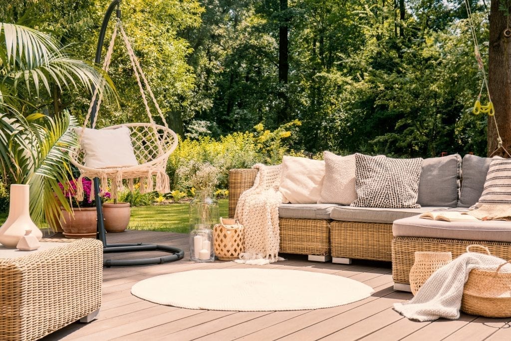An outdoor, wooden patio framed by sofas, a swing chair and a cream coloured, round outdoor rug.